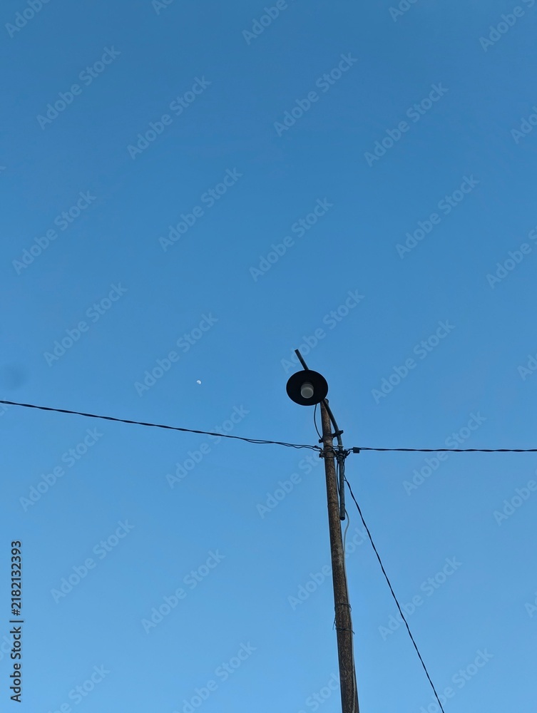 Obraz premium Old rustic street lamp pole against a clear blue sky with a small moon visible in the daylight