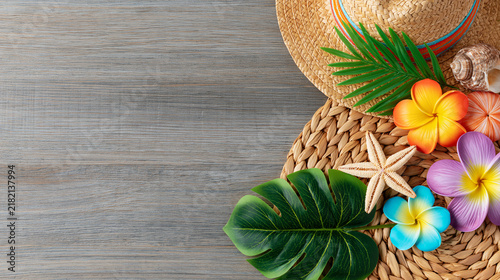 Tropical beach accessories including straw hat starfish and colorful plumeria flowers on wooden background for travel ads.