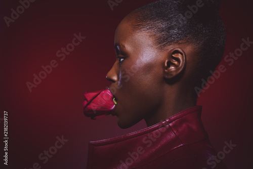 Foto Profile of a dark skinned African woman holding a red rose in her mouth wearing a red leather jacket