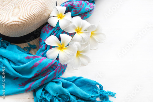 white flowers frangipani, hat and blue scarf of lifestyle woman relax autumn season arrangement flat lay style on background white 