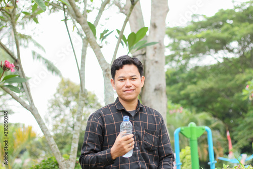 Фотография A young Indonesian man after drinking water; a young Asian man wearing a flannel shirt and staying hydrated with water