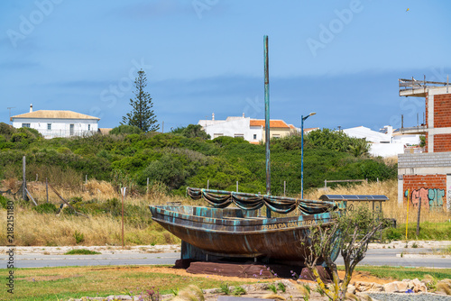 Canvas Print A weathered bronze boat sculpture with a tall mast and decorative netting stands as a coastal monument near white village houses