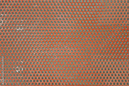 Orange perforated metal sheet texture background with circular hole pattern.