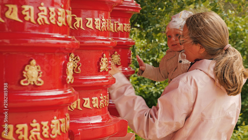 Fotografie Mother infant interacting with vibrant red prayer wheels featuring golden Tibetan script