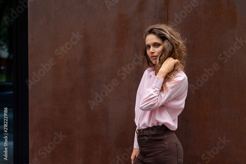 Young woman touching her curly hair against brown wall looking at camera