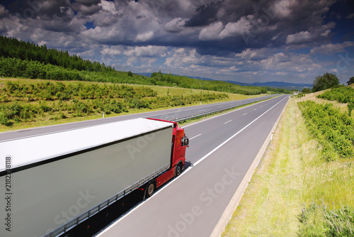 A truck on a highway drives through a wide landscape, transporting goods