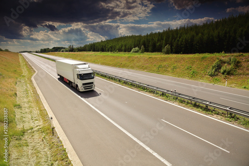 A truck on a highway drives through a wide landscape, transporting goods