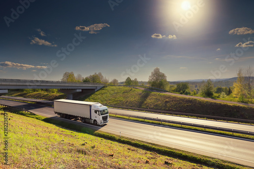 A truck with semi-truck drives through a wide landscape at sunset
