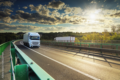 A truck with semi-truck drives through a wide landscape at sunset