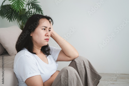 Фотография Stressed Asian woman holding her head at home, feeling anxious and depressed abo