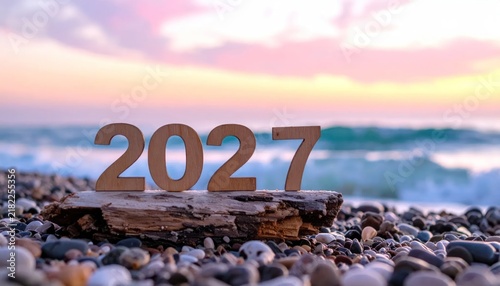Wooden 2027 numbers on pebble beach at sunset.
