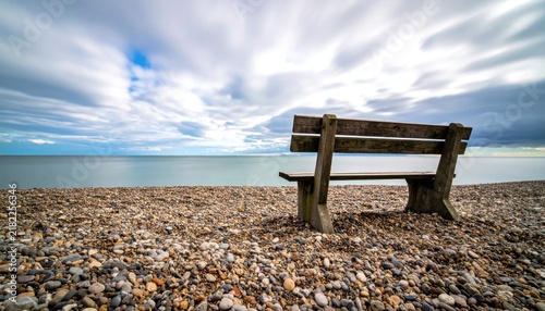 Wooden bench on pebble beach facing calm sea.