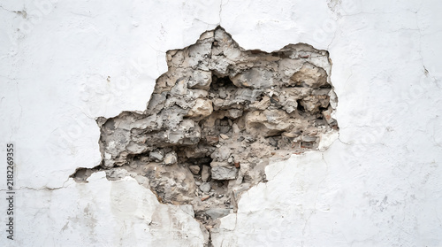 Hole in White Plaster Wall Revealing Rough Stone