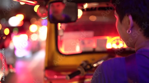 Tuk tuk driver navigating through vibrant neon city streets at night in Bangkok.