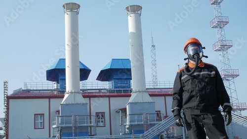 Obraz na plátně Protective suited man stands before industrial plant, wearing gas mask and helmet with focused expression