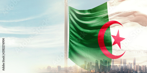 Fotografía Algeria national flag wavering in beautiful clouds with building skyline