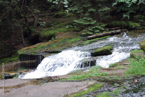 Beautiful mountain waterfall cascade of Szklarka stream flowing over wide granite plates in a green forest