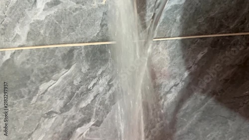 Clear Stream of Water Pouring Against Tiled Bathroom Wall