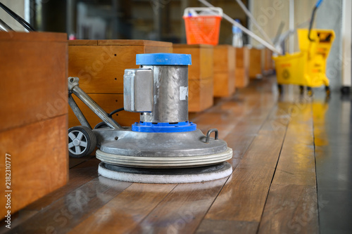 Worker cleaning and polishing wooden floor using professional floor cleaning machine in modern interior. Concept of hygiene, maintenance, cleaning service, and janitorial work in building.