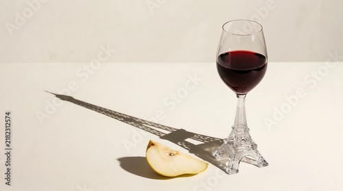 Red wine glass with tower shaped stem and artistic shadow, fresh pear on beige. French wine culture and tasting concept