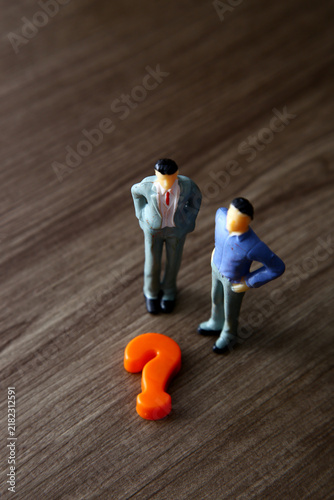 Miniature businessmen pondering a question mark, facing decision