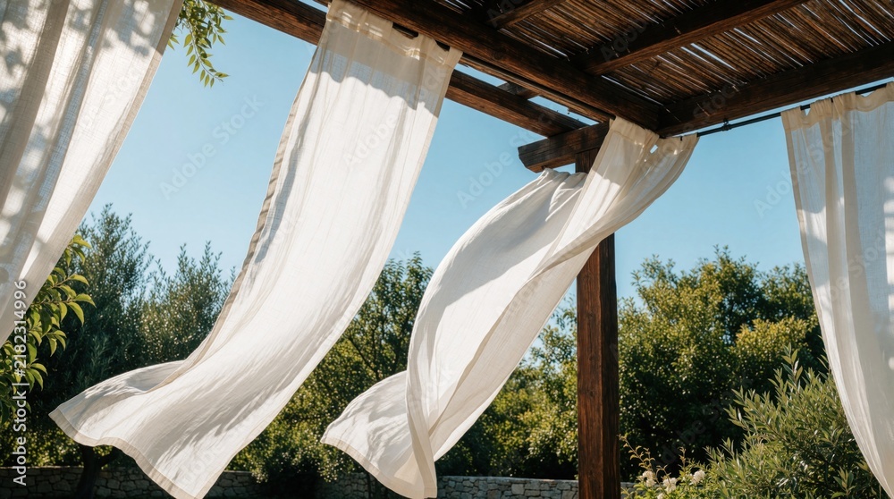 Obraz premium White fabric curtains gently flutter on a wooden pergola against a clear blue sky. Lush green trees surround the outdoor space, creating a serene ambiance for relaxation and enjoyment.