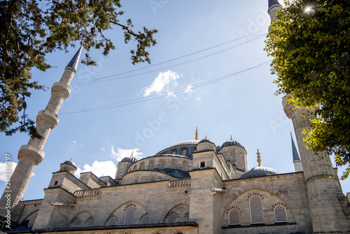 Fotografie Historic Ottoman mosque building stands under bright blue sky framed by tree leaves