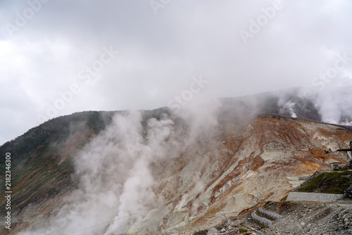 Obraz na płótnie 活発な火山活動を示す大涌谷の壮大な風景。荒涼とした斜面から白煙が勢いよく立ち上り、雲が低く垂れ込める劇的な自然の景色。