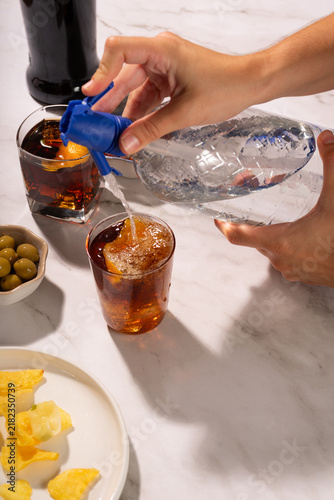 Obraz na plátně Hand serving soda from a siphon on a glass with vermouth, ice and a twist of orange