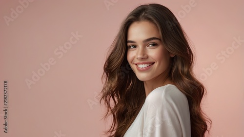 Cheerful young woman with long wavy hair smiles warmly against a pastel pink backdrop.