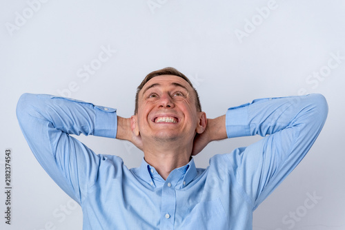 Canvastavla Cheerful adult man in a blue shirt is relaxing with his hands behind his head, s