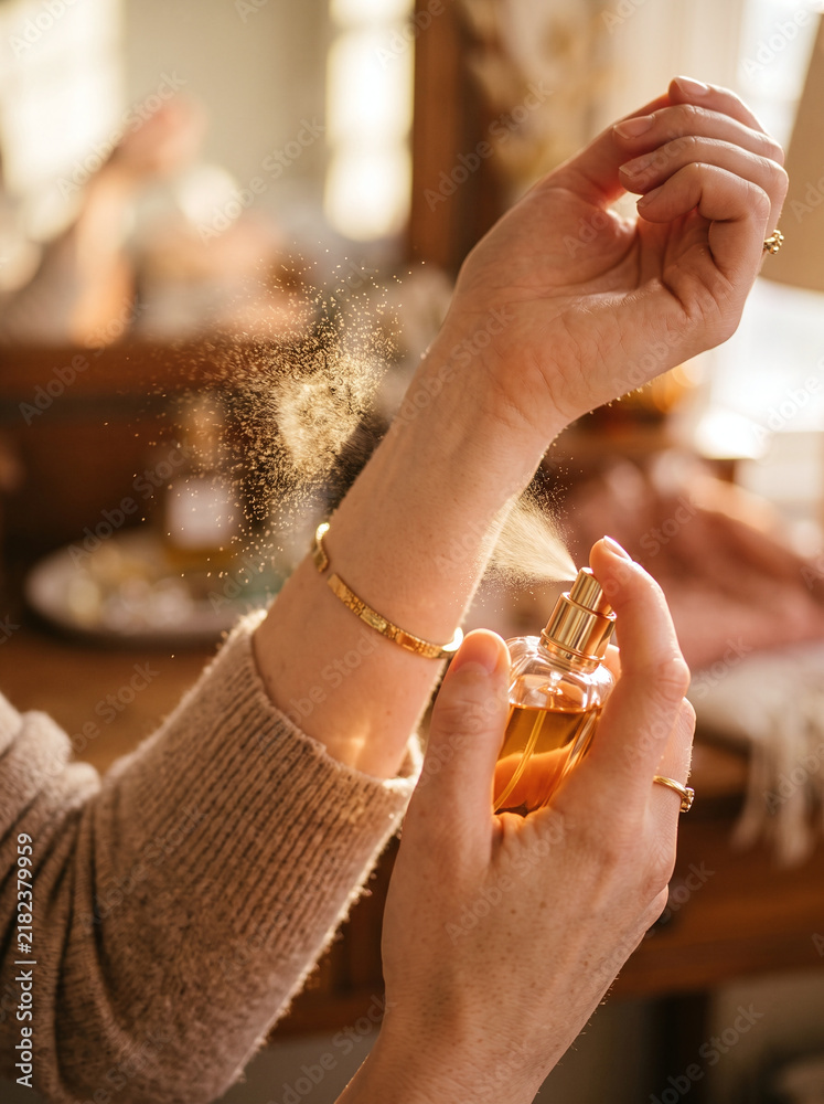 Obraz premium Woman spraying luxury fragrance mist onto her wrist in warm golden light