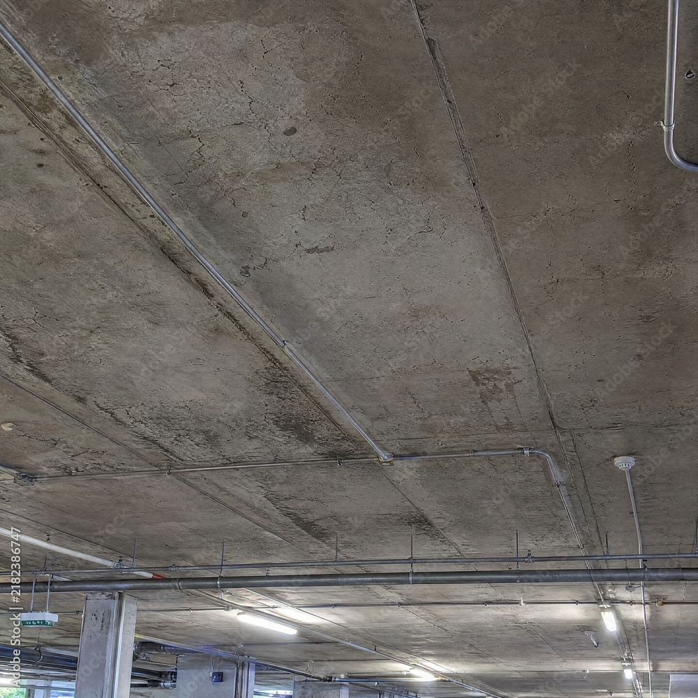Obraz premium Concrete ceiling with exposed pipes and lighting in a parking garage 