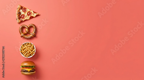 A top-down view of a delicious fast food meal featuring a slice of pepperoni pizza, a salty soft pretzel, a small bowl of crispy golden french fries, and a classic cheeseburger on a coral background