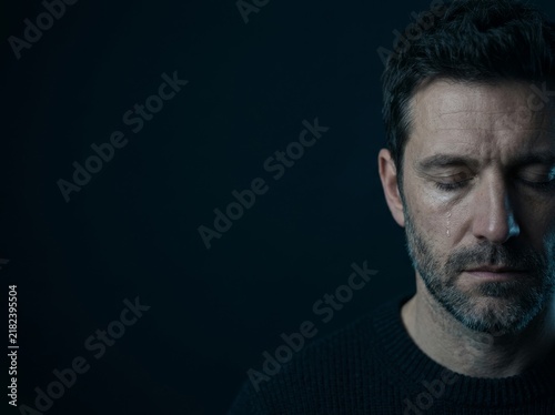 Emotional close-up of a man with tears running down his face against a dark backdrop.