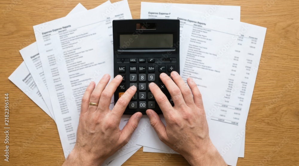 Fototapeta premium Hands using a calculator over financial expense reports on wooden desk