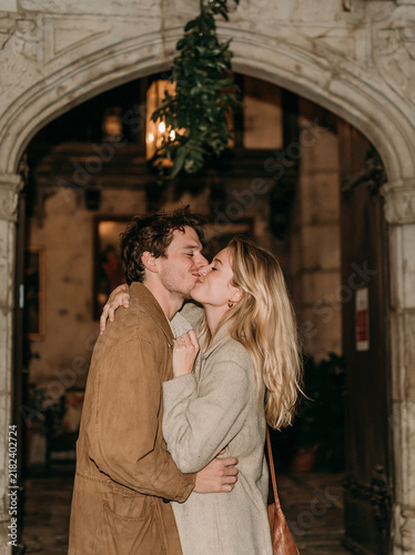 Romantic young couple kissing passionately under a historic stone arch decorated with festive greenery