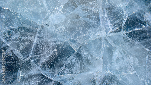 Cracked ice texture with frozen blue patterns, macro shot of crystalline ice surface, abstract winter background for seasonal design