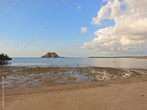 Fotografie Peaceful tropical coastline at low tide with a small rocky island, calm blue sea
