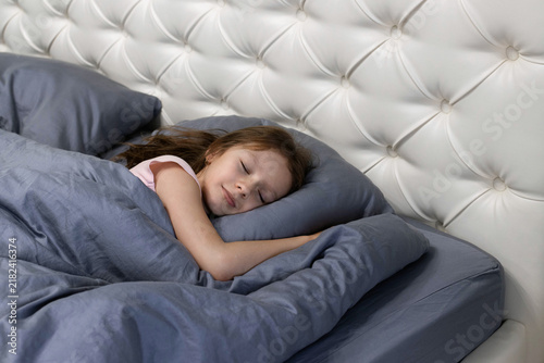 A little girl sleeps on a large bed in a bedroom with a modern renovation. The concept of waking up in the morning and starting a new day