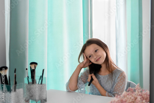 A smiling little girl pretending to do makeup at a vanity mirror, holding a cosmetic brush. Child play, imitation of beauty routines, innocence, self-expression, and creativity at home