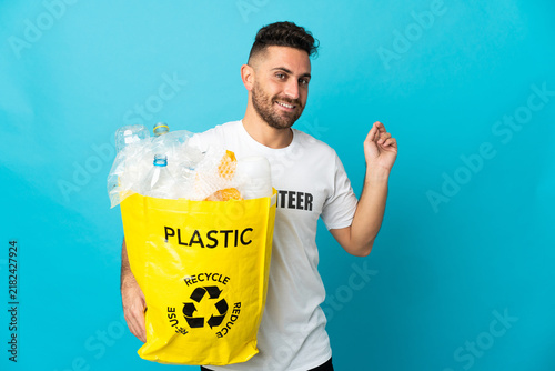 Foto Caucasian man holding a bag full of plastic bottles to recycle isolated on blue