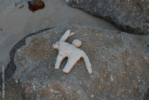 Foto A discarded handmade cloth effigy used as a symbolic ritual object sits flat against a textured coastal rock on a beach in Maputo