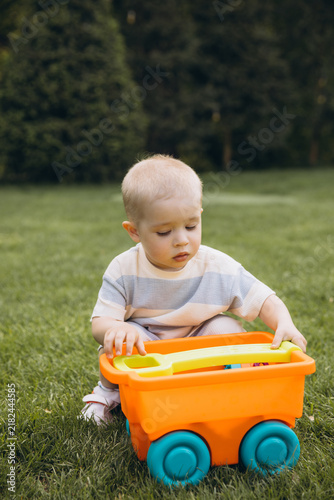 Obraz na plátne Toddler playing with a colorful toy wagon on green grass, enjoying childhood pla