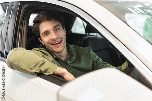 Photography Smiling Young Caucasian Male Sitting Inside Car With Window Open, Enjoying Drive In Urban Environment