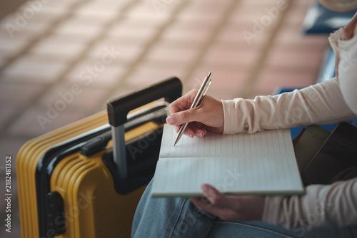 Фотография Traveler writing notes in a notebook beside a suitcase at an airport, representing travel planning, itinerary preparation, vacation organization, and journey preparation