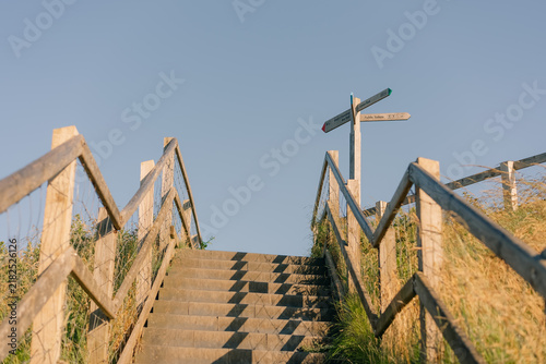 Canvas Print Wooden staircase with handrails leading up a grassy hillside under a clear blue sky - 4 September 2026