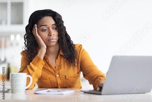 Worried Black Woman In Her 30s Working On Laptop At Home Office  Resting Her Head On Hand While Struggling To Focus On Task. Modern Workspace Creating Business Concept.