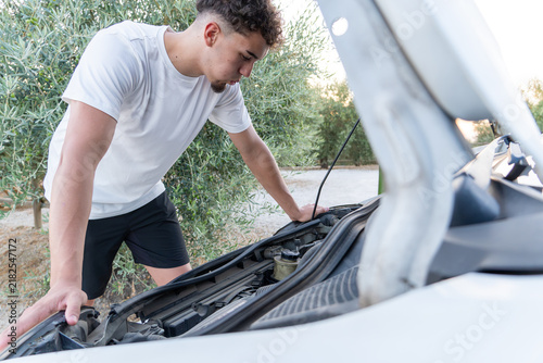 Fotografie Young man standing by a broken down car on the roadside, looking into the open h
