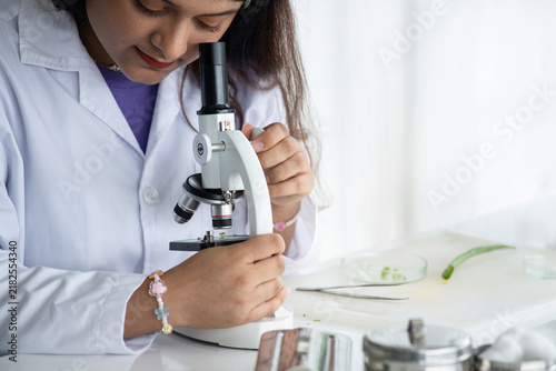 Young female student conducting a science experiment using a microscope in a laboratory, representing science education, STEM learning, scientific research, discovery and hands-on learning.